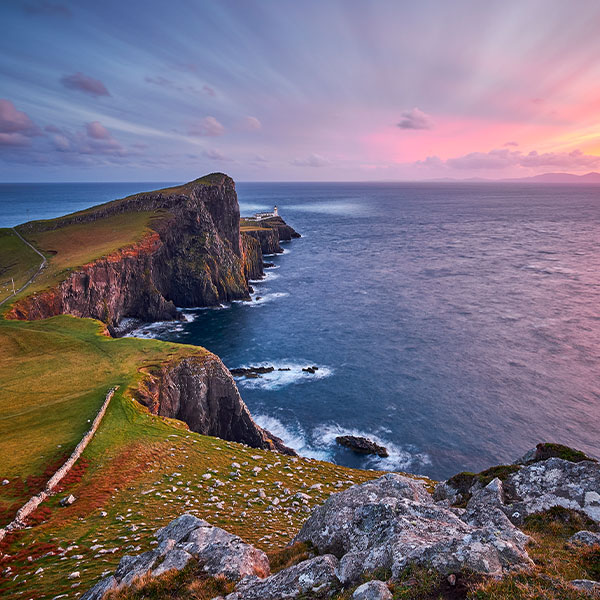 Looking towards a lighthouse and the sea at sunset from the rugged cliffs of the Isle of Skye
