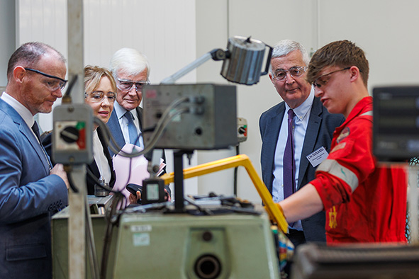 Four people watch on as a student demonstrates equipment. Four people watch on as a student demonstrates equipment.