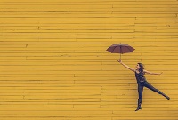 A person holding an umbrella in front of a yellow wall