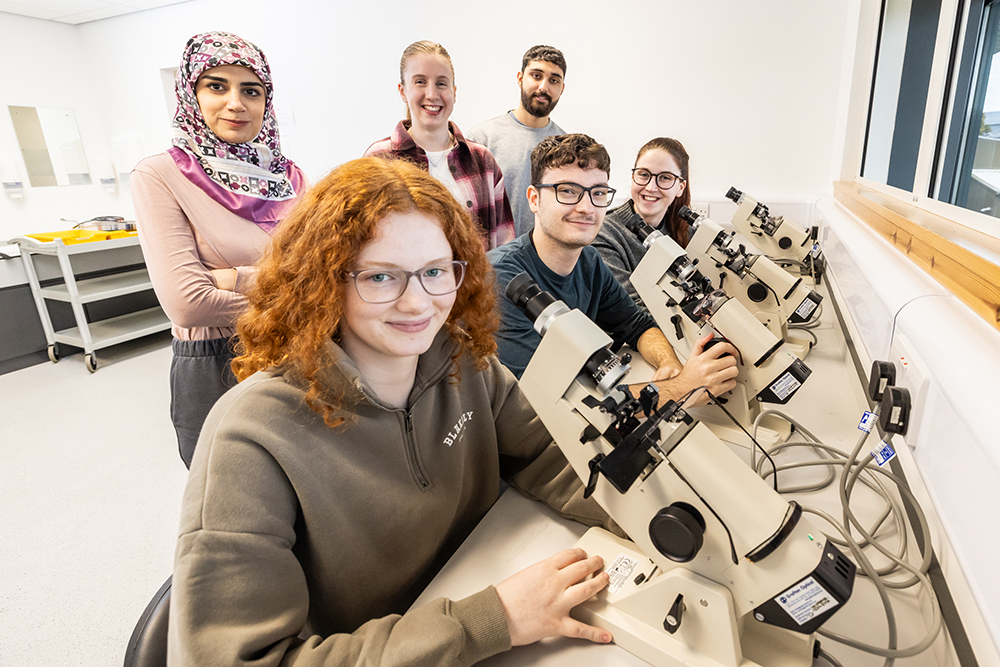 Optometry students posing in front of optometry equipment Optometry students posing in front of optometry equipment