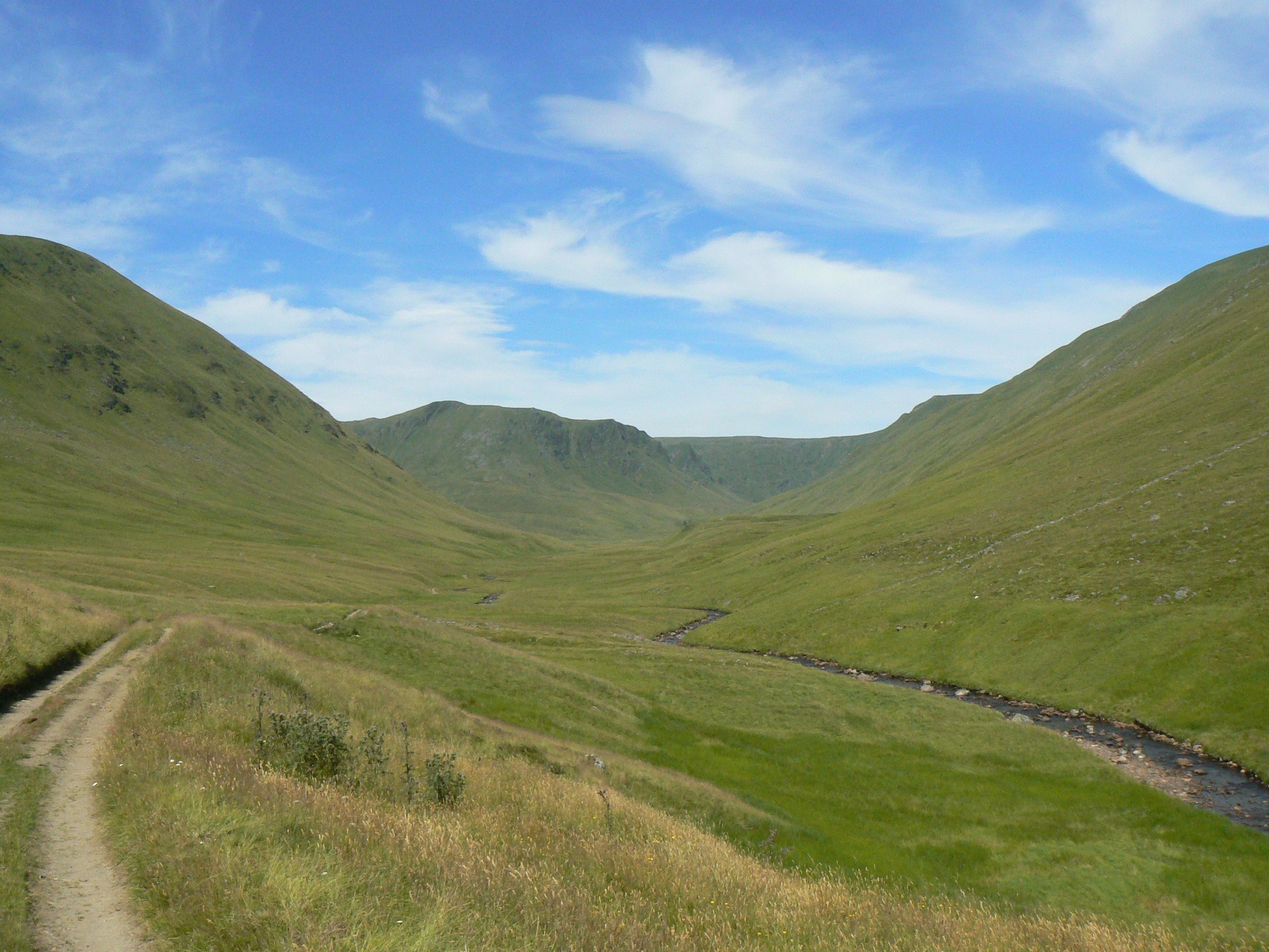 A peaceful valley with green grass and a winding stream, surrounded by rolling hills under a clear sky