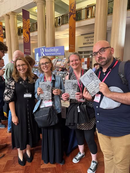 Group of eight people holding books, standing in front of a banner showing the logo for Routledge publishers.