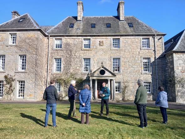 Group of people standing in front of a large stone country house. Group of people standing in front of a large stone country house.