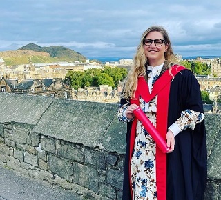 Woman in graduation robes with Edinburgh skyline behind