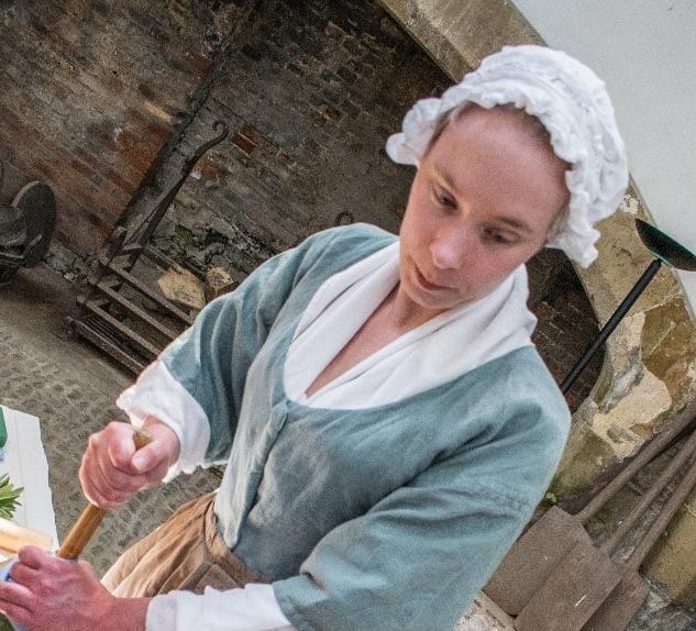 Woman dressed in 18th-century clothing including an apron and bonnet churning butter