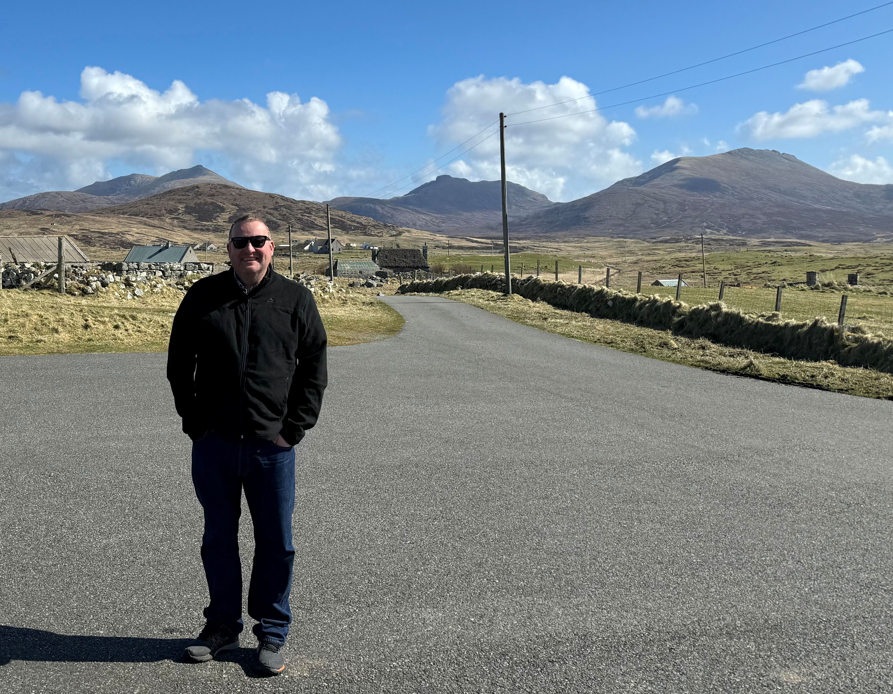 Person standing on a rural road with mountains and blue sky in the background. Person standing on a rural road with mountains and blue sky in the background.