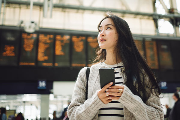 Young aspirational student arriving at a train station, with arrivals and departures board in the background Young aspirational student arriving at a train station, with arrivals and departures board in the background